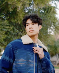 a young man standing in front of a tree wearing a blue jacket and white shirt