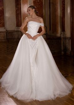 a woman in a white wedding dress standing on a wooden floor with her hands on her hips