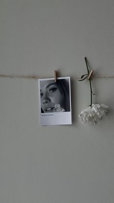 a white flower hanging from a clothes line next to a photo on a wall with a string