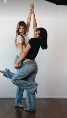 two young women are dancing together on the floor in front of a white wall and wooden floors