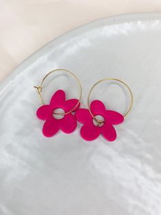 two pink flowers are attached to gold hoop earrings on a white plate with a light background