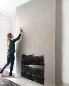 a woman standing next to a fireplace in a living room with a wall mounted fire place