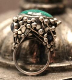 Add a unique touch to your jewelry collection with this stunning handmade abstract ring. The ring features a beautiful cabochon-shaped malachite gemstone, set in sterling silver. The green-colored ring is a perfect accessory for any occasion. The ring is crafted in the United States and has a ring size of 8. The secondary stone, sapphire, adds to the uniqueness of the ring. The malachite cabochon is the main attraction, but the sapphire stone adds an extra sparkle to the piece. The ring is perfect for those who appreciate fine jewelry and want to add a unique touch to their collection. Green Gemstone Cabochons Fine Jewelry, Green Emerald Cabochon Rings, Modernist Round Cabochon Jewelry, Elegant Green Chrysocolla Jewelry, Artisan Green Chrysocolla Rings, Unique Oval Cabochon Emerald Ring, Unique Oval Emerald Ring With Polished Finish, Silver Malachite Gemstone Ring, Green Malachite Rings With Polished Finish