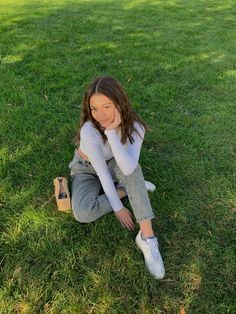 a woman sitting in the grass with her hand on her chin and looking at the camera