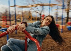 a young woman is swinging on a red swing set at a park with her long hair blowing in the wind