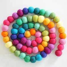 multicolored felt balls are arranged on a white surface, with a hook in the middle