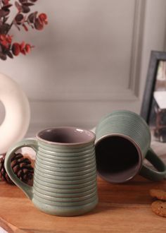 two green mugs sitting on top of a wooden table next to cookies and a vase