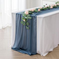 the table is covered with blue and white linens, flowers and greenery on it