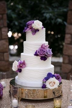 a wedding cake with purple and white flowers on the top is sitting on a table