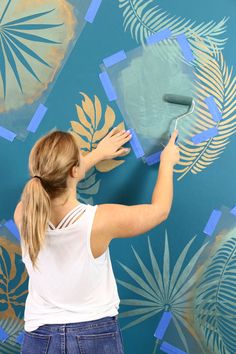 a woman is painting a wall with blue and gold leaves on the walls behind her