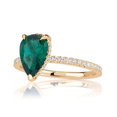 a pear shaped emerald and diamond ring in yellow gold with diamonds around the band, on a white background