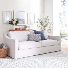 a living room with a white couch and some pictures on the wall above it, along with a basket full of flowers