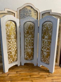 three white and gold painted wooden frames with decorative designs on the sides, sitting on a wood floor