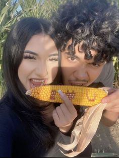 two people posing for a photo while holding a corn cob in front of their face