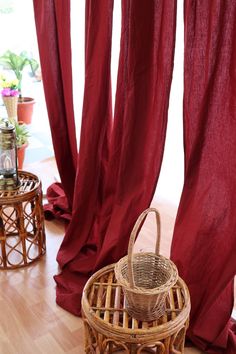 a wicker basket sitting on top of a wooden floor next to red drapes