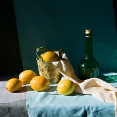 some lemons are sitting on a table next to a glass bottle and a towel