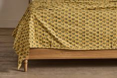 a bed with a yellow bedspread on top of it and wood flooring