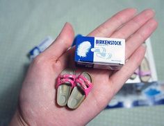 a person holding two pairs of pink shoes in their hand and a box of toothpaste