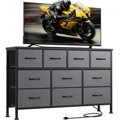 a television mounted on top of a dresser next to a large screen tv with a motorcyclist