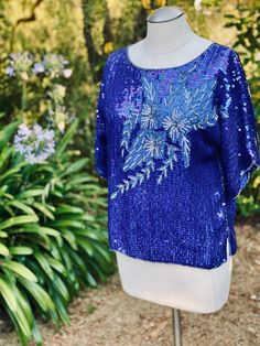 This is a vibrant blue floral sequin top blouse that is perfect with Jeans or a dressed up pant. The fabric is pure silk with sequin embellishment. This lovely top is made in India by Jasmine by K.V.M. Calif.  Measurements laying flat across: Pit to pit-22" Waist- 20" Length- 22.5" Sleeves- 13" Festive Embellished Blue Blouse, Festive Blue Embellished Blouse, Blue Contrast Sequin Fabric For Spring, Blue Sequin Fabric With Contrast Sequin For Spring, Blue Sequin Fabric With Contrast Design For Spring, Embellished Tops For Summer Festivals, Embellished Summer Tops For Festive Occasions, Blue Sequin Fabric For Summer Night Out, Embellished Tops For Summer Festivities