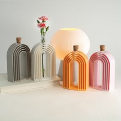 three different colored vases sitting next to each other on a white surface with a pink flower in the middle