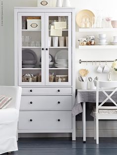 a white china cabinet sitting next to a table with plates and cups on top of it