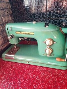 an old green sewing machine sitting on top of a red table next to a brick wall