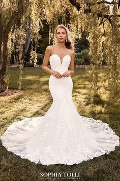 a woman in a wedding dress standing under a tree with her hands on her hips