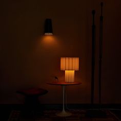 a table with a lamp on it next to a chair and lampshade in the dark