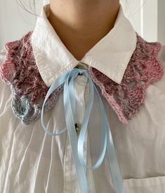 a woman wearing a white shirt with blue ribbon around her neck and pink crocheted collar