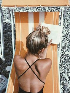 a woman laying on top of a beach chair next to an open book in her hand