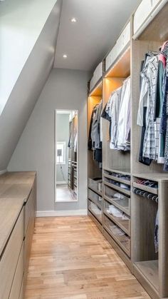 a walk in closet with lots of clothes on shelves and wooden flooring, along with an open door leading to another room