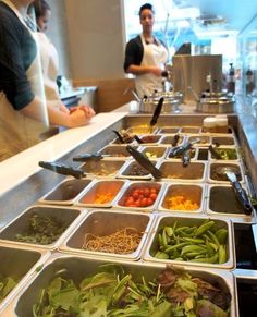 people are preparing food in trays on the counter at a restaurant, while another person stands behind them