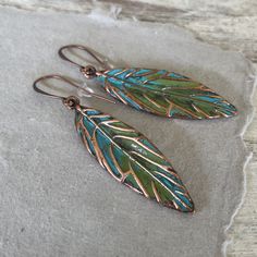 These hand painted artsy copper leaf earrings are a unique and striking accessory that have been crafted in our island studio using a special house patina paint blend resulting in a beautiful blue green finish reminiscent of the Caribbean sea. Once the patina process is complete, we buff and seal the copper for durability and to prevent tarnishing. Each pair of earrings are one-of-a-kind, with variations in the patina that add to their handmade charm. Size: 2.50 Inches from Lobe Ear Wire: Choice Artistic Hand Painted Copper Earrings, Hand Painted Copper Artsy Earrings, Hand Painted Copper Bohemian Earrings, Hand Painted Artsy Copper Earrings, Artsy Hand Painted Copper Earrings, Bohemian Hand Painted Copper Earrings, Artsy Hand Painted Copper Jewelry, Green Hand Painted Copper Earrings, Hand Painted Green Copper Jewelry