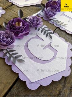 purple paper flowers are placed on top of white cards with the letter c in them