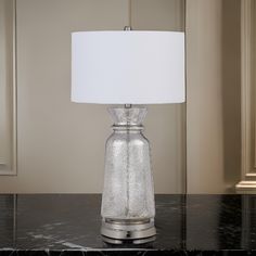 a glass lamp sitting on top of a black table next to a white lampshade