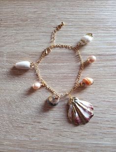 a bracelet with seashells and pearls hanging from it's gold chain on top of a wooden table