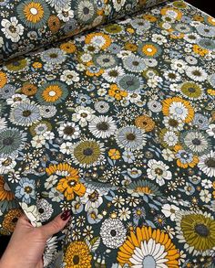 a woman's hand is touching the fabric on a floral print tablecloth with yellow, green and white flowers