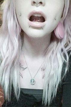 a close up of a person with pink hair and piercings on her nose,