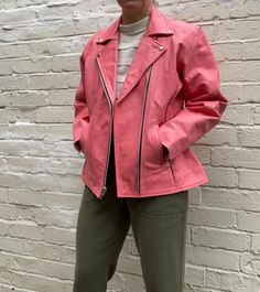 "Bright salmon pink leather motorcycle leather jacket with braiding and gathering at the waist. The leather is grained and is very stiff in movement and appearance. Zips up at the front and has two side pockets. Black quilted lining. Inside open pocket. Zips on the back of the sleeves. Best fit a UK 10-12 Label at neck: L Genuine Leather Label inside: Echtes Leder. Real Leather. 100% Polyester lining.  Made in Pakistan. Measurements: Shoulder to shoulder 45 cm Chest 105 cm Waist 86 cm Hips 110 c Pink Biker Outerwear For Spring, Pink Biker Jacket For Fall Workwear, Pink Biker Outerwear For Fall, Pink Leather Jacket For Fall, Pink Leather Jacket With Zipper For Fall, Pink Long Sleeve Biker Jacket For Work, Pink Biker Jacket For Workwear, Pink Leather Jacket With Zipper Closure For Fall, Pink Winter Biker Jacket