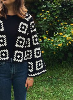 a woman standing in front of a bush wearing a black and white knitted sweater