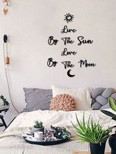 there is a bed with pillows and plants on the floor in front of it that says, live by the sun, love by the moon