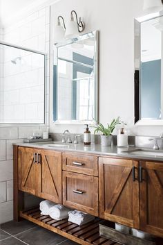 a bathroom with two sinks, mirrors and a wooden cabinet in the middle of it