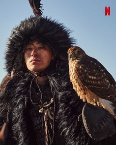 a man with an eagle headdress on holding a bird in his hand and looking at the camera