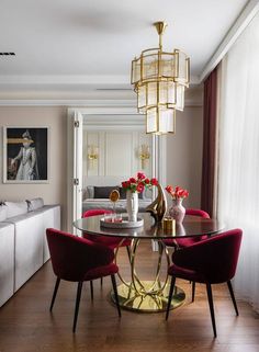 a dining room table with red chairs and a chandelier hanging from the ceiling