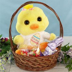 a yellow stuffed chicken sitting in a basket filled with candy and candies next to flowers