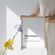 a woman holding up a framed poster with the words, these defense on it and flowers in front of her