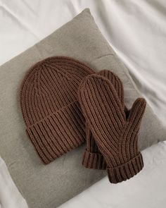 two knitted mittens laying on top of a pillow next to a gray pillow