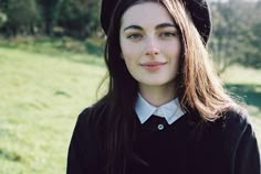 a young woman with long hair wearing a black sweater and hat standing in a field