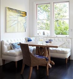 a white couch sitting next to a table in a living room under two large windows